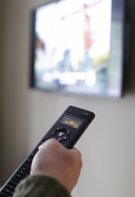 Universal remote held in user's hand, pointing at TV in soft focus